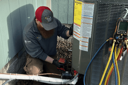 An A&amp;E technician bends down to fix an outdoor residential HVAC unit.