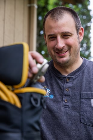 An A&E Plumbing tech pulls out a tool from his bag, a smile on his face as he prepares a solution for a plumbing issue.