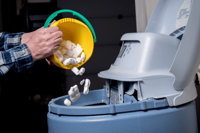 A homeowner pours salt in a water softener system.
