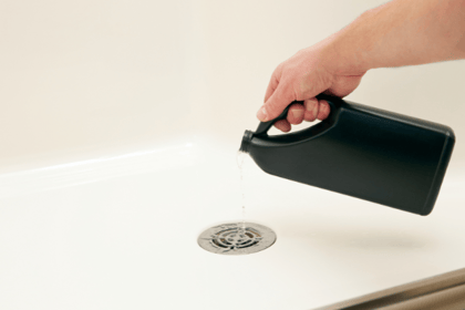 A hand pours a chemical drain cleaner into a residential drain.