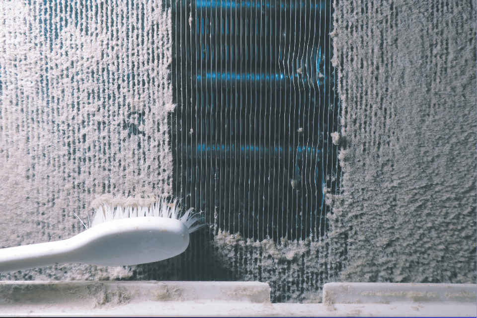 A brush clears away a buildup of dirt and dust on an HVAC air filter.