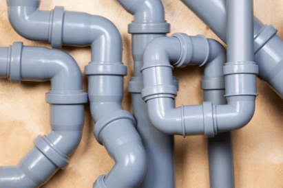 A pile of grey residential PVC pipe for indoor plumbing sits against a brown background.