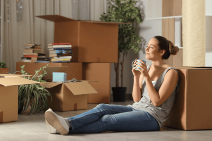 Woman relaxing on a box with a coffee mug in hand, appearing relaxed in her home.