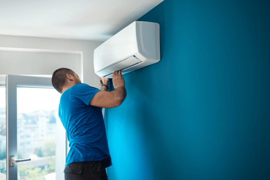 Man adjusting indoor mini-split system on blue wall.