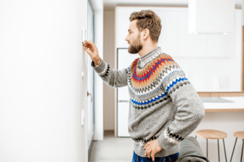 Man in colorful, striped sweater standing in front of an indoor wall thermostat, presumably to check his IAQ data.
