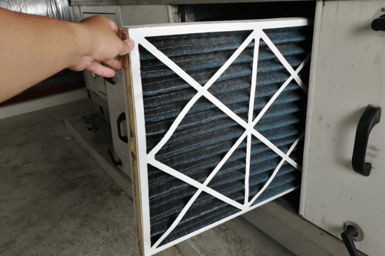 A hand pulling out an HVAC filter directly from the HVAC unit, showing the surface area and pleats a filter offers.