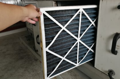 A hand stabilizes a HEPA filter as it's taken out of an HVAC unit.