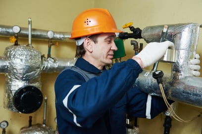 A plumber wraps heat tape around a commercial plumbing system pipe.