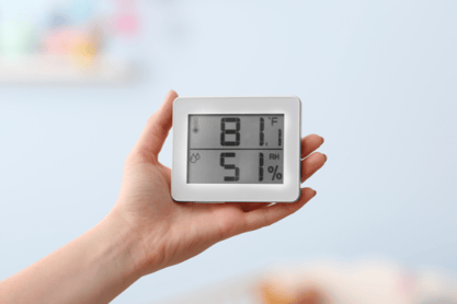 A hand holds out a digital display indicating the temperature and humidity.