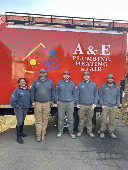 A shot of the A&amp;E Plumbing, Heating and Air plumbing team standing in front of a red company van.