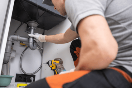 A plumber works on a laundry drain plumbing fixture.
