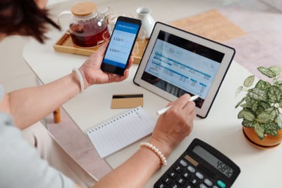A person sits in front of their computer with a calculator and a phone with their bank app, going over their PGE/Gresham utility bill.
