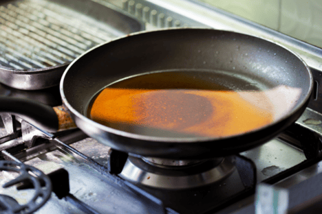 A pan sits on a residential oven with a thin layer of grease coating the bottom.