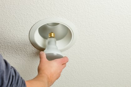 A person reaches to install a light in a recessed light.