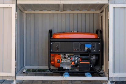 A red/orange electrical generator sits in a large shed, sheltered from the elements.