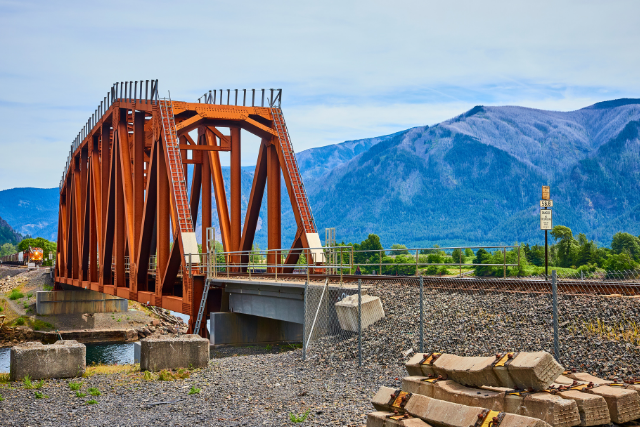 A rusted, steel train bridge in Stevenson, WA is contrasted with dark blue hills in the background.