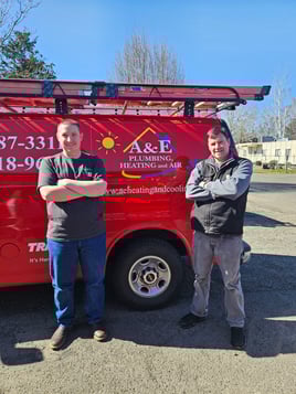 Two A&amp;E Plumbing, Heating and Air Techs stand in front of a red company van.