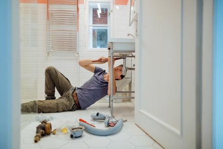 A man performs plumbing maintenance under a bathroom sink.