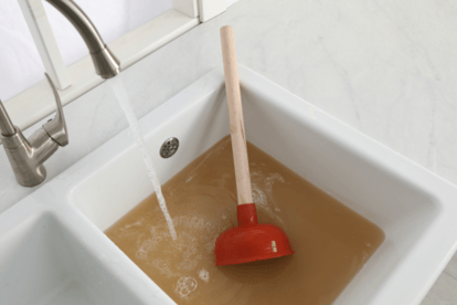 A plunger sits in a clogged utility sink with the water running in an effort to begin the unclogging process.
