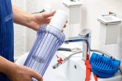A plumber holds a filtration system in his hands before installing it in a homeowner's bathroom sink.