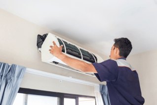 An HVAC tech steps on a ladder to inspect a wall-mounted HVAC unit.