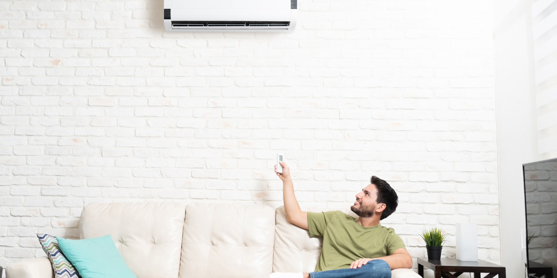 Man adjusting temperature on an HVAC mini-split while sitting on the couch, showing how easy total temperature control is. 